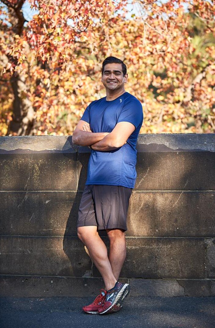 Dilruk Jayasinha stands with arms folded, leaning against a wall wearing running clothes, smiling widely.