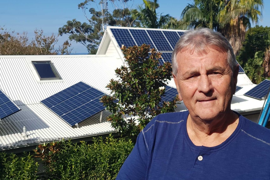 Rex Leighton in front of his house, which has solar panels on the roof.