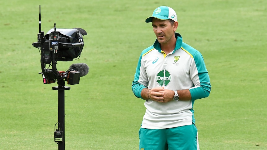 An Austrlaian cricket coach stares into a camera while giving a TV interview on the ground during a Test match.