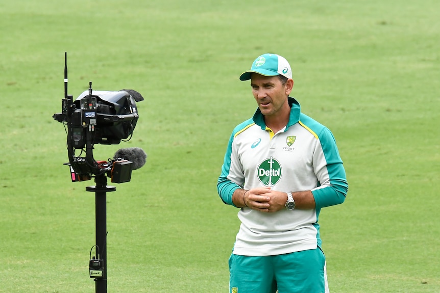 An Austrlaian cricket coach stares into a camera while giving a TV interview on the ground during a Test match.