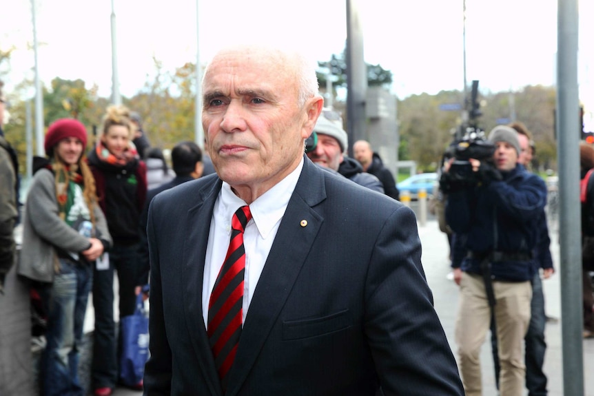 A man in a suit walks past a crowd.