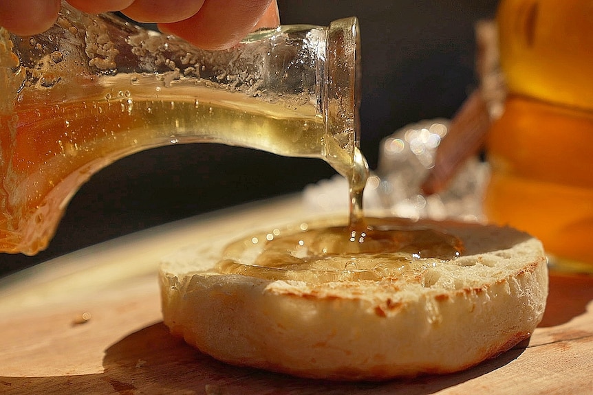Golden honey poured onto a crumpet out of a jug. 