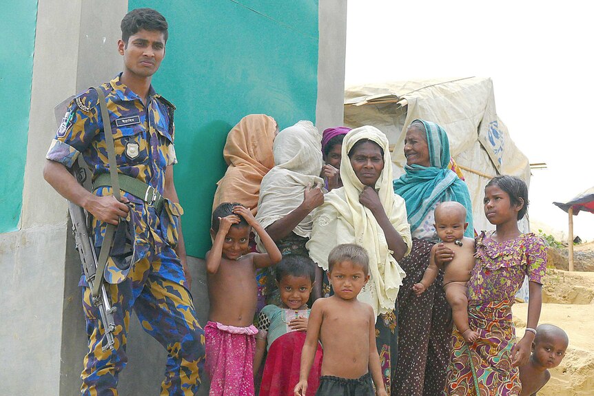 A young solder stands next to a group of refugees