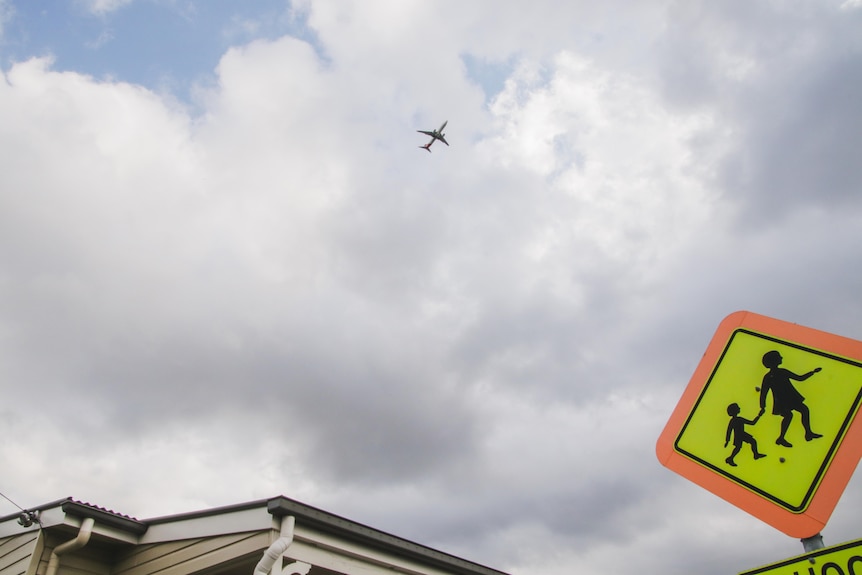 A plane over a house. A children crossing sign can also be seen. 