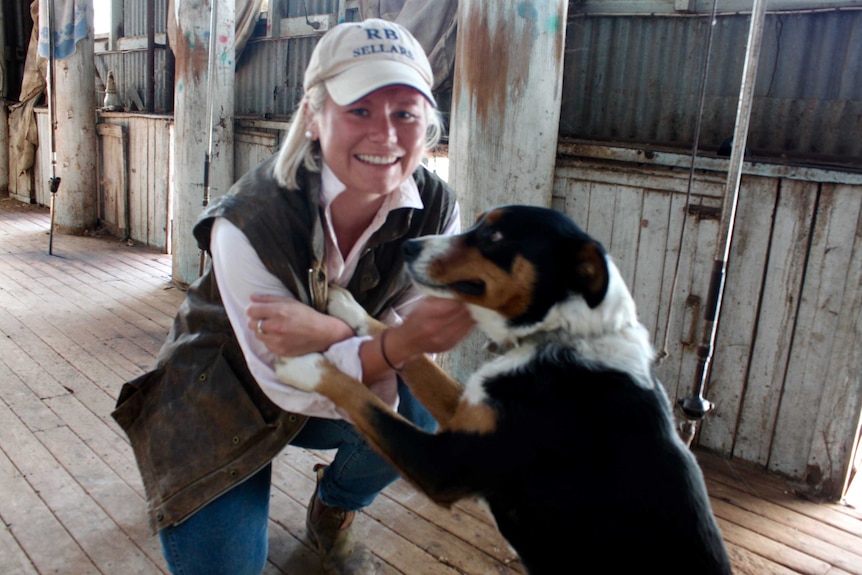 Smiling woman in shearing shed with sheepdog