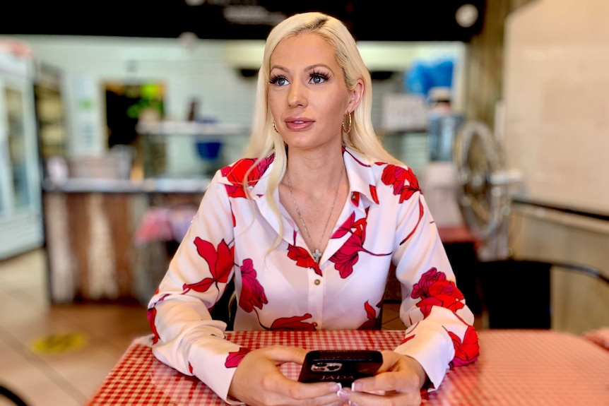 A woman sits in front of a pizza shop counter.