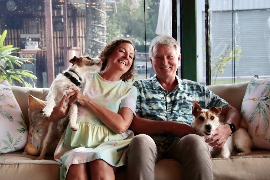 Middle-aged woman and man sitting on a couch smiling at the camera, petting two dogs