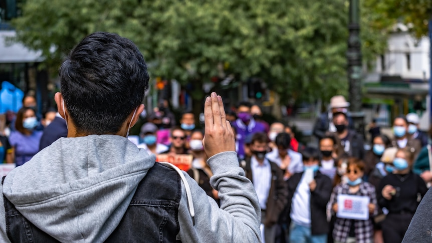 The back of a person shown giving a three-finger salute in front of a crowd.