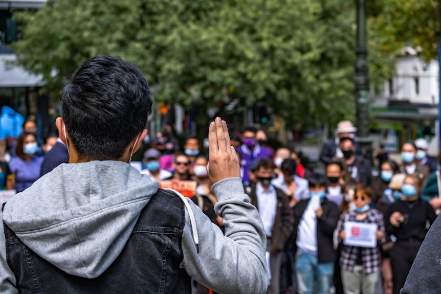 The back of a person shown giving a three-finger salute in front of a crowd.