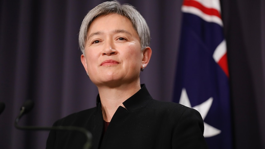 Wong smiles slightly, an Australian flag visible behind her.