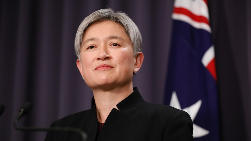 Wong smiles slightly, an Australian flag visible behind her.