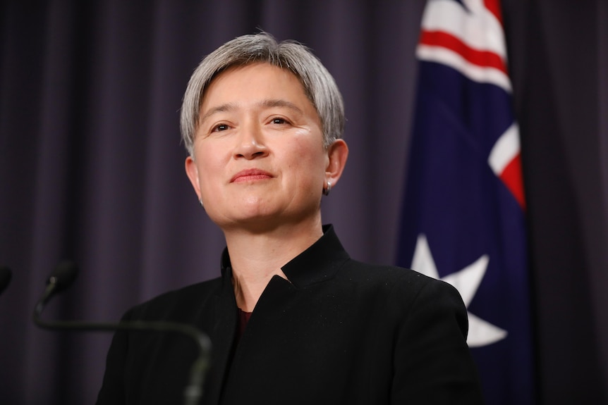 Wong smiles slightly, an Australian flag visible behind her.