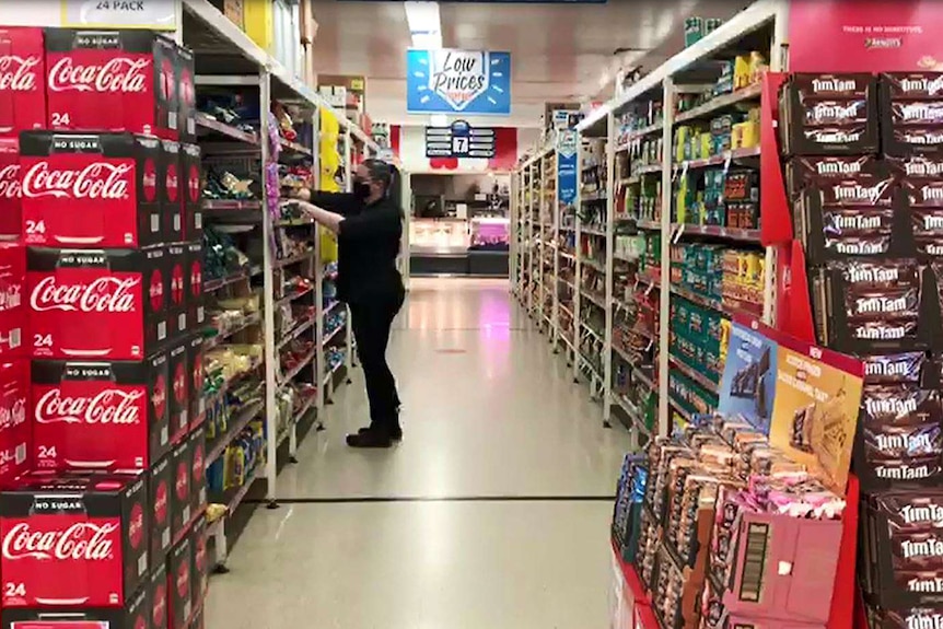 A woman reaches into a supermarket shelf.