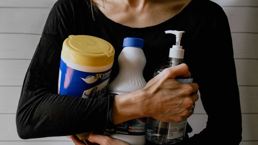 Woman holding cleaning products in arms.