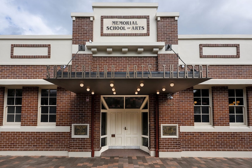 The front entrance to the Sutherland Arts Theatre with brown brick and white facade with vertical lettering on the awning.