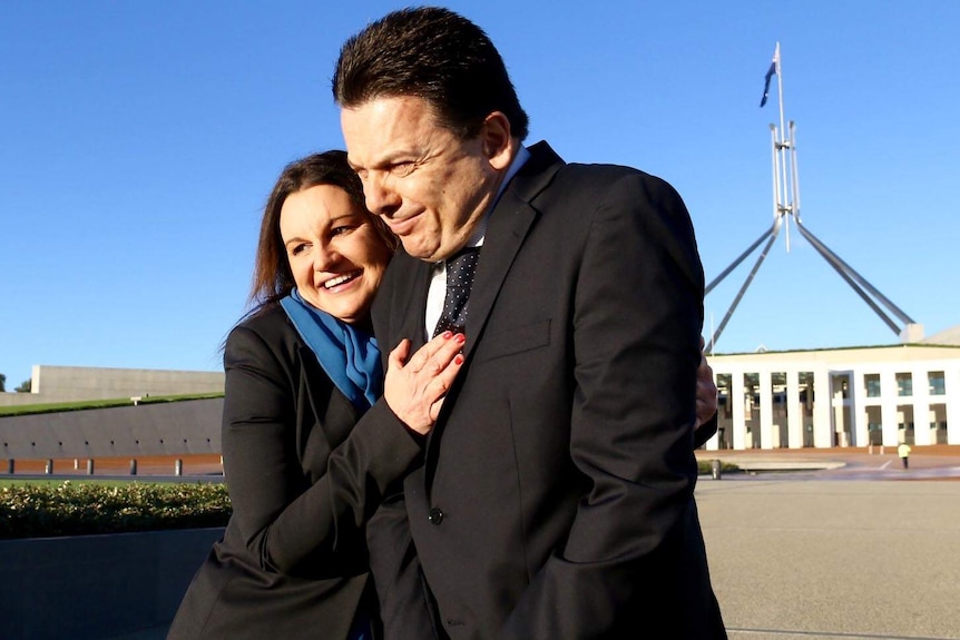 Jackie Lambie hugs Nick Xenophon outside Parliament House in Canberra, the flagpole visible behind them.
