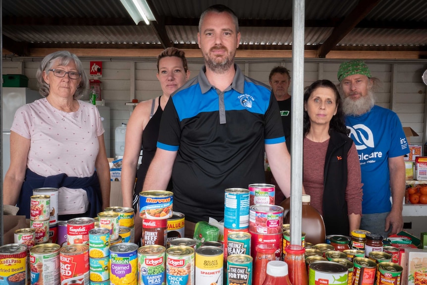 Several people stand behind a table full of canned vegetables.