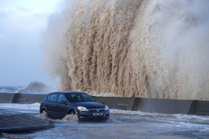 A car drives along a flooded road in New Brighton.