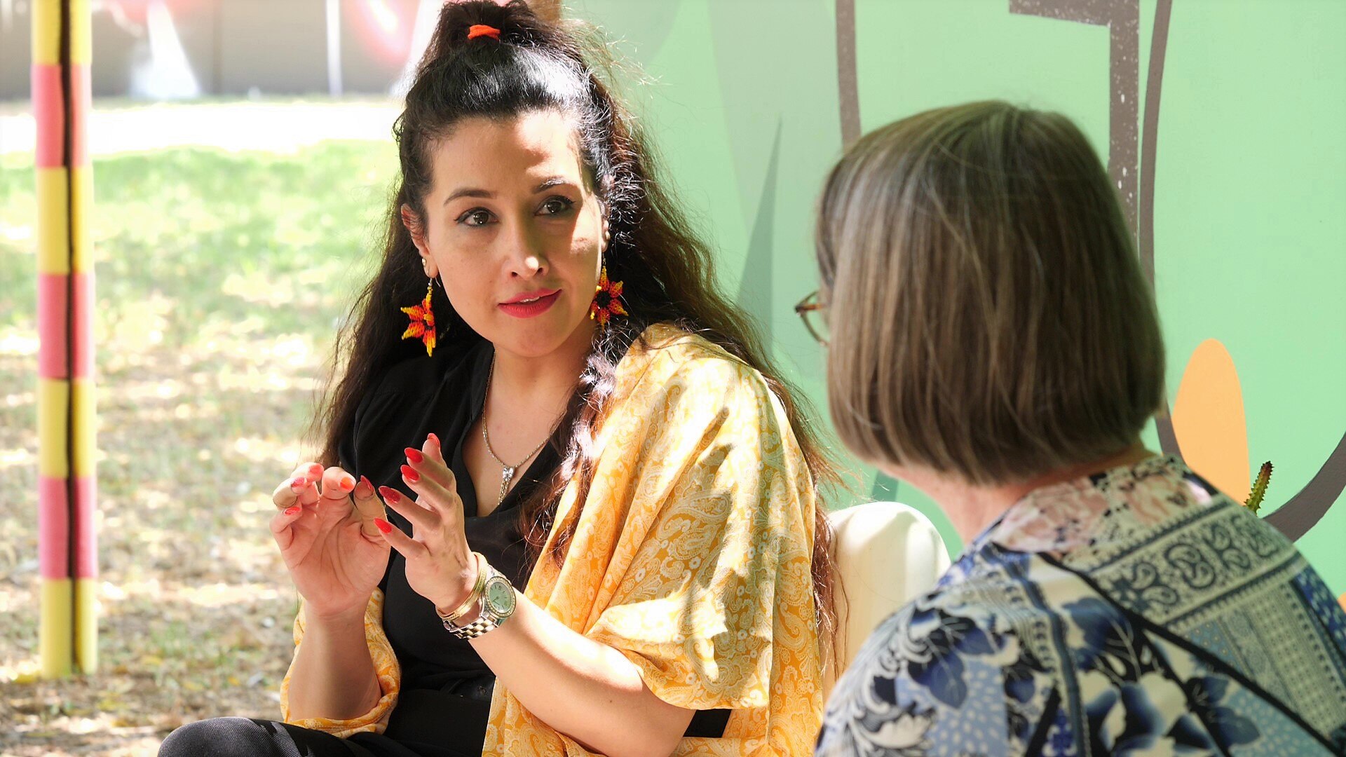 Women speak to each other in garden. 