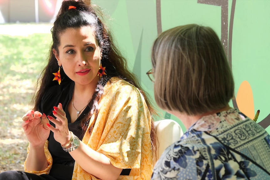 Women speak to each other in garden. 