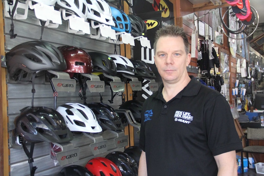 A man stands in front of a display of bike helmets in a bike shop.