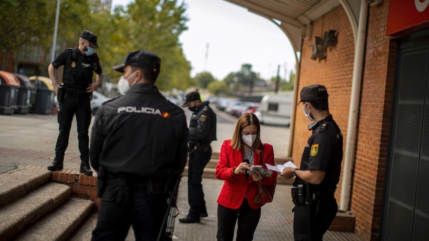 Uniformed police question a woman and inspect her documents and mobile phone outside a train station