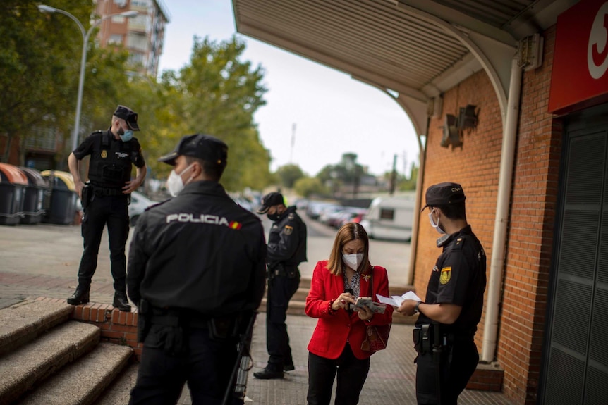 Uniformed police question a woman and inspect her documents and mobile phone outside a train station