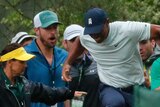 Tiger Woods grimaces and hops away as a crowd of spectators react behind him