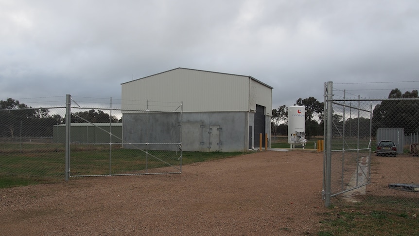 A shed in a paddock with a high fence around it.