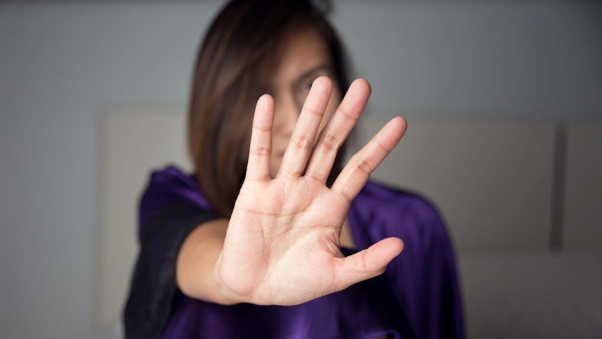 A woman in purple pyjamas holds up her hand to the camera to signify stop the violence