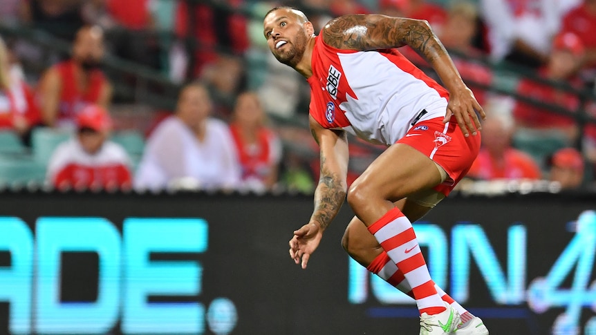 A Sydney Swans AFL player bends his body as he watches a shot on goal.