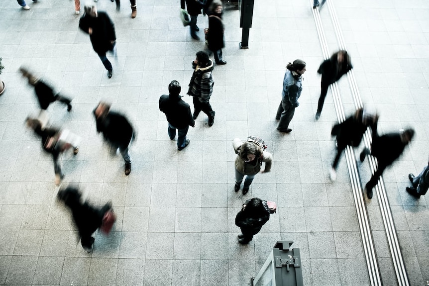 Looking down at people walking in an open space, some blurred by the slow shutter speed.