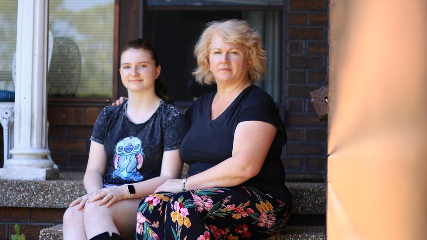 A middle aged woman sitting on the step of a house with her teenage daughter