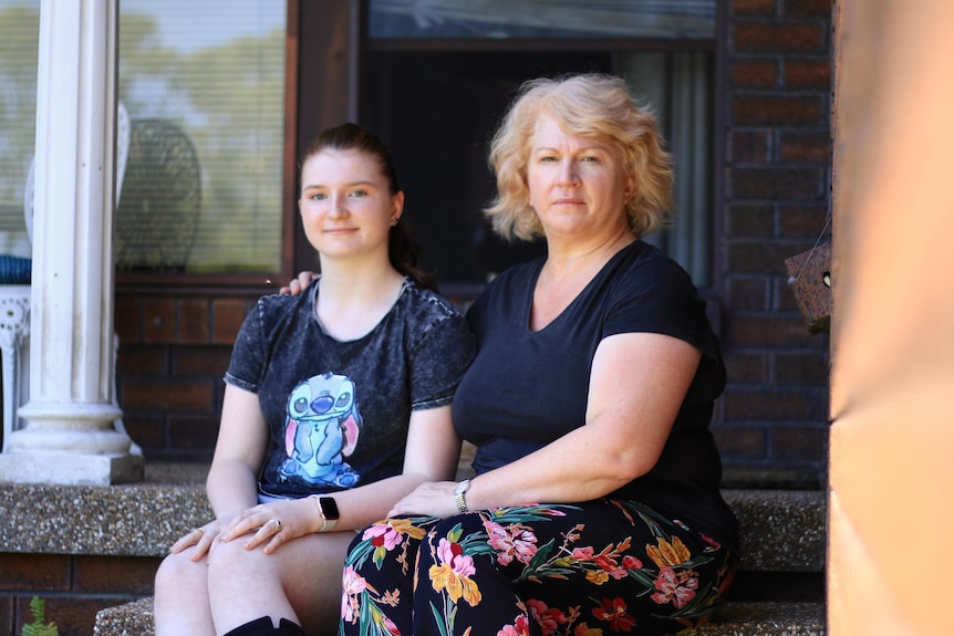 A middle aged woman sitting on the step of a house with her teenage daughter