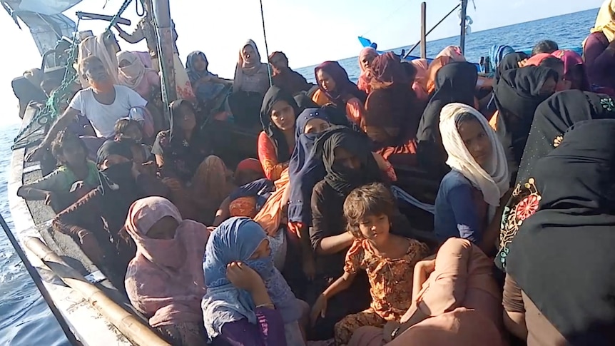 Dozens of people including children sit aboard a small boat