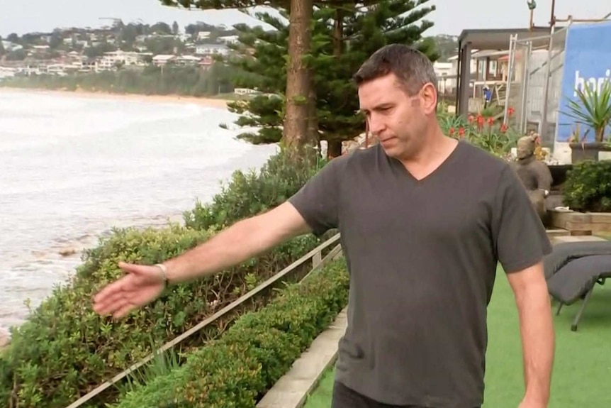 A man stands in his beachfront yard and points towards the ocean.