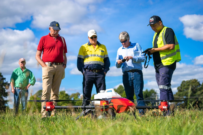 A group of men standing around looking at a drone sitting on the ground.