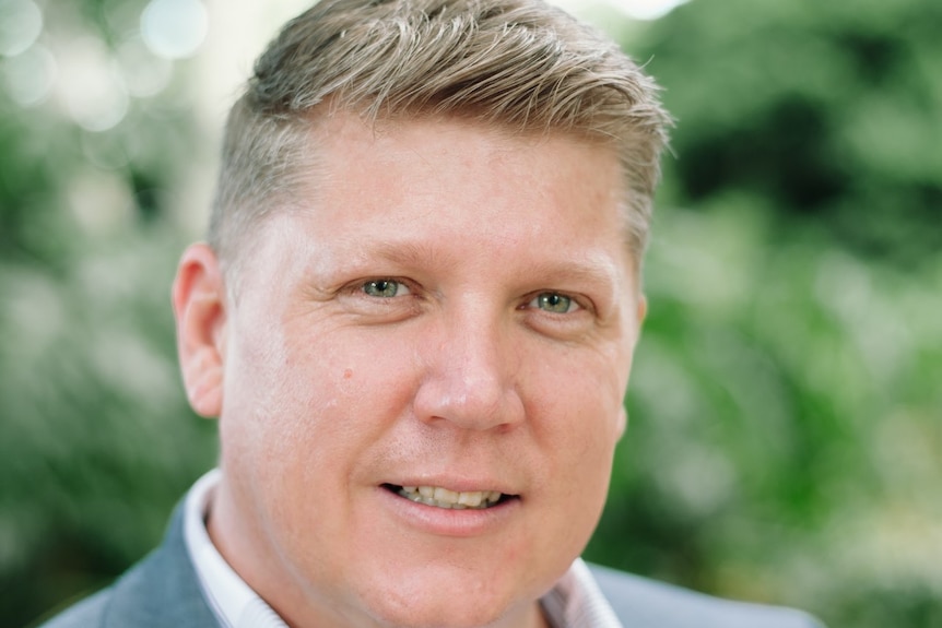 Middle aged man with blond crew cut smiles at camera