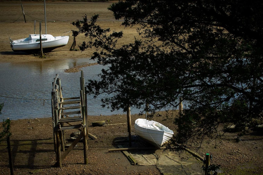 A dinghy and a small sailing boat sit in the mud at low tide.