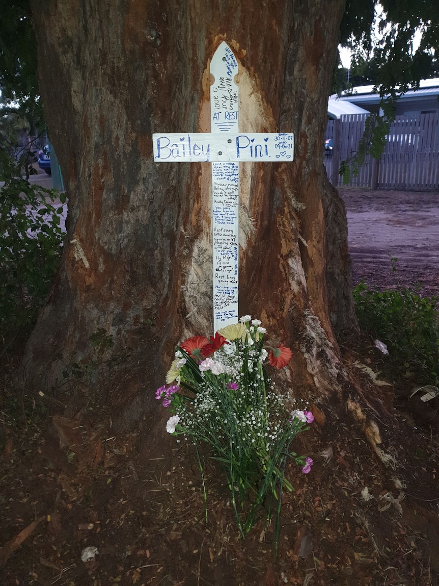 a white cross with bailey pini's name on it in front of a tree