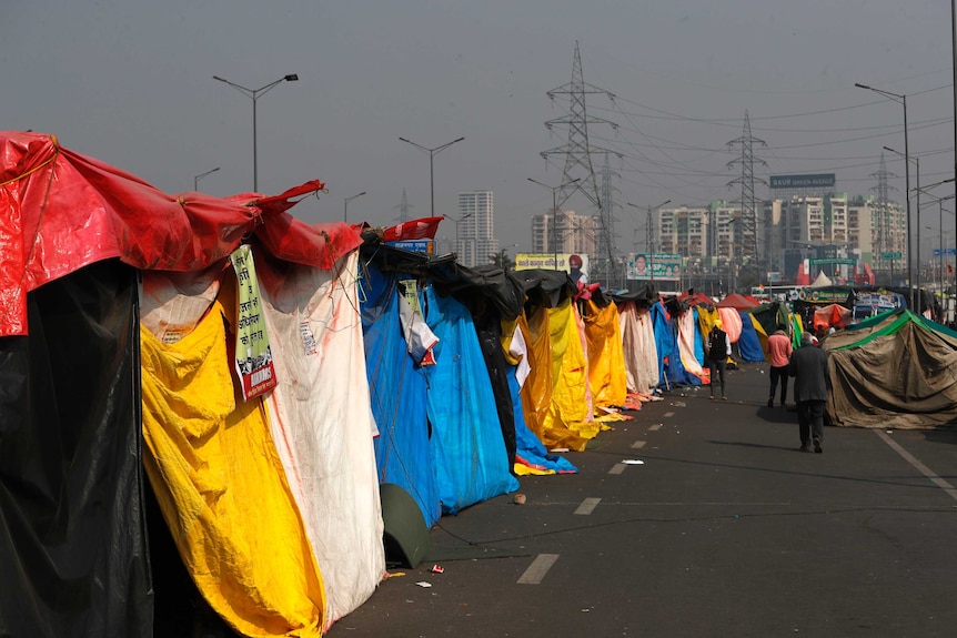 A line up of different coloured tents on a highway with people walking past.