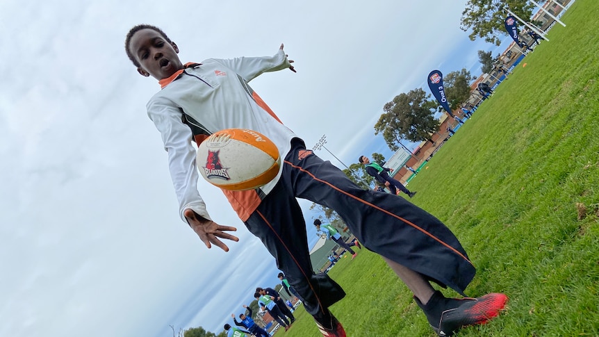 A boy in a white and orange jacket and dark pants kicking a football