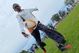 A boy in a white and orange jacket and dark pants kicking a football