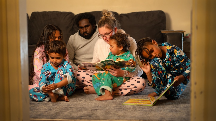 A family sits around and reads a book.