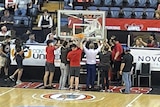 People stand holding up a basketball net and backboard.