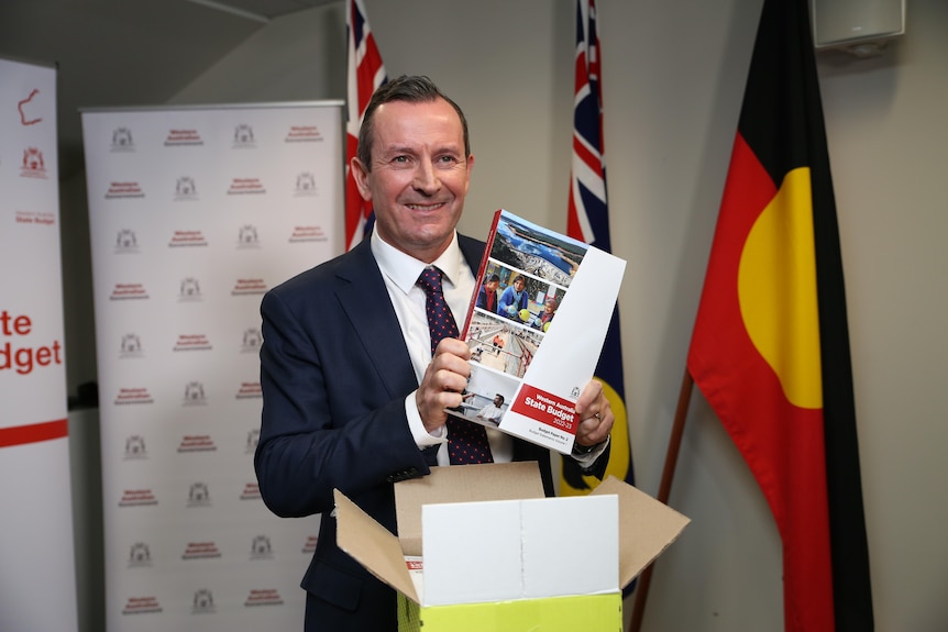 Mark McGowan smiles while holding the budget papers