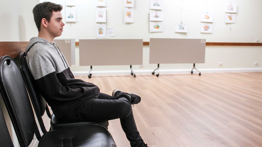 Matthew sits on a chair in a community hall.