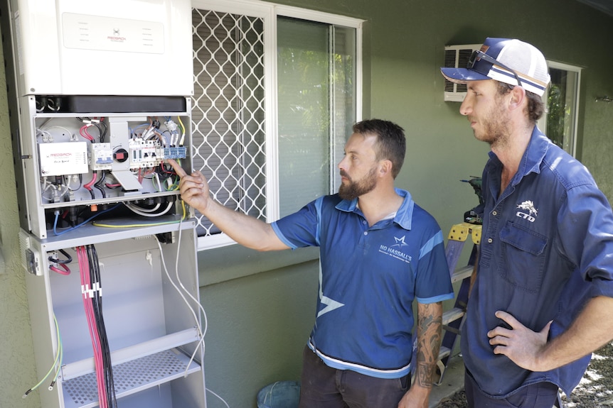 two men in tradesmen clothing with a household battery