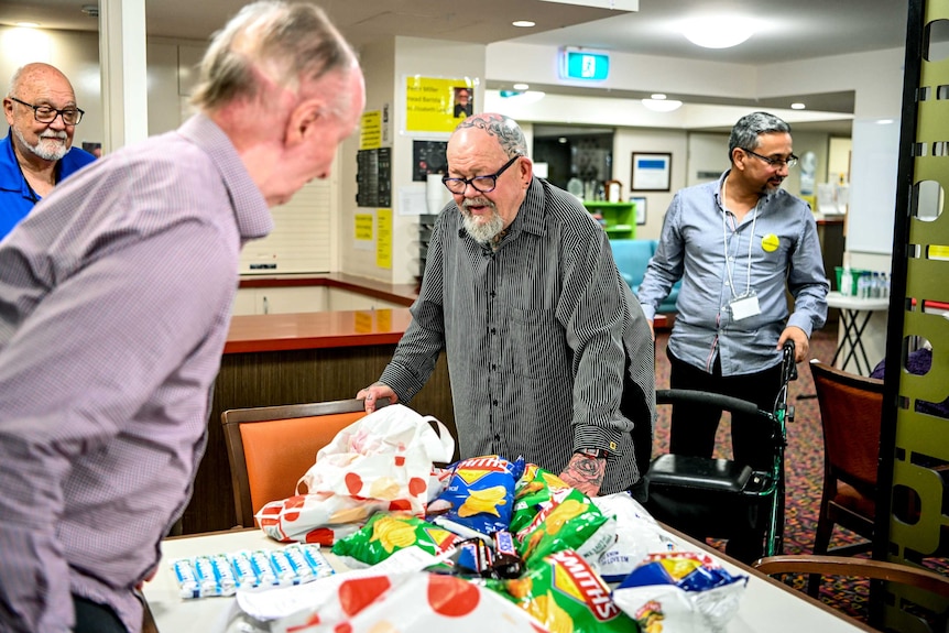 Geoffrey Ostling with three other men in a communal area of his aged care home, with chips on the table.