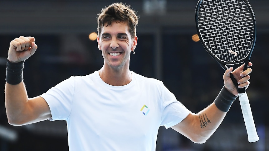 Thanasi Kokkinakis holds his hands and racquet up and smiles